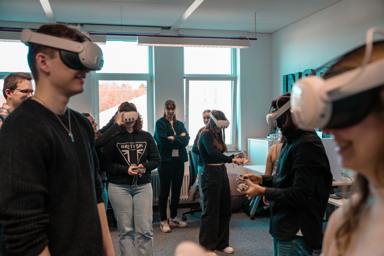 who-we-are A group of diverse adults using VR headsets in an office setting.