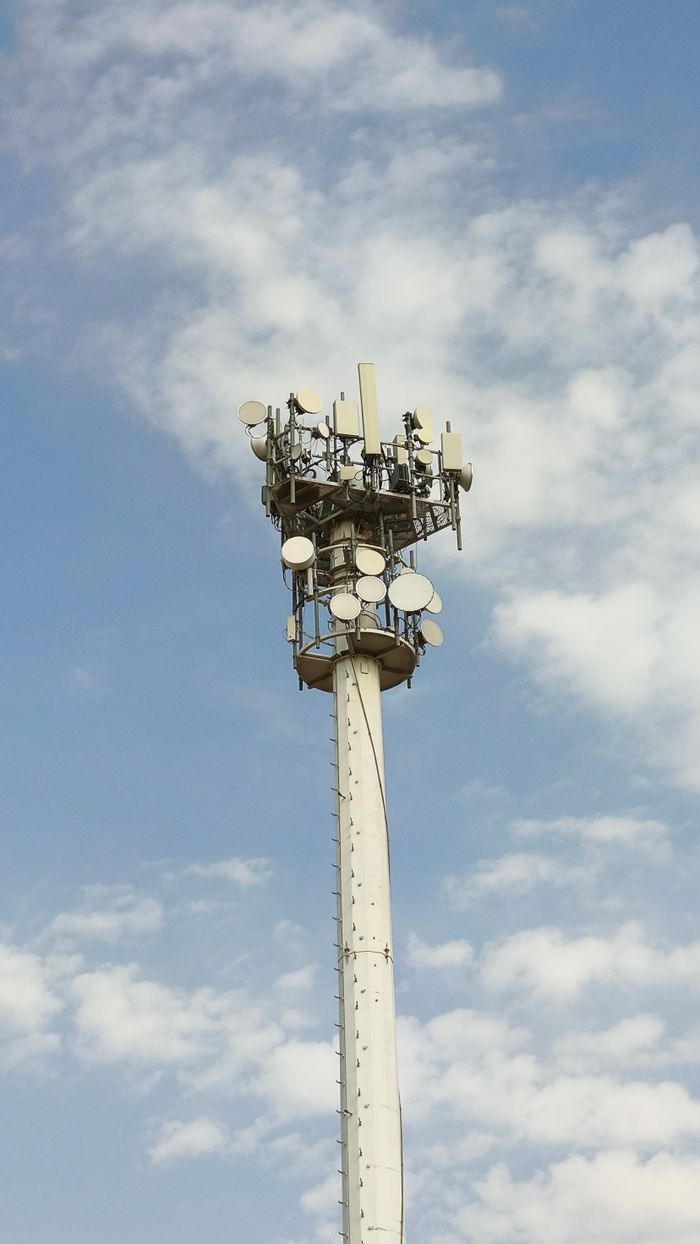 about-us A tall telecommunications tower with antennas under a blue sky with clouds.