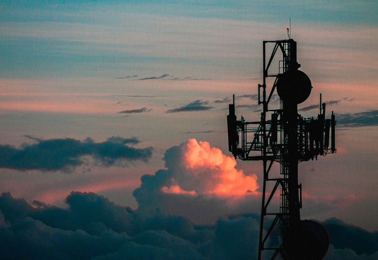 services-03 A communication tower silhouette against a colorful sky with vibrant sunset clouds.