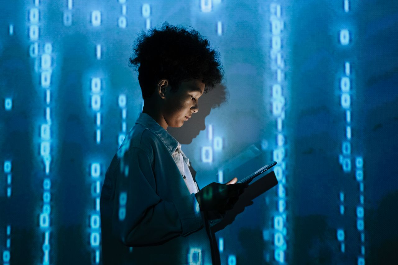 our-story Teenage boy with a tablet surrounded by digital binary code in a studio setting.